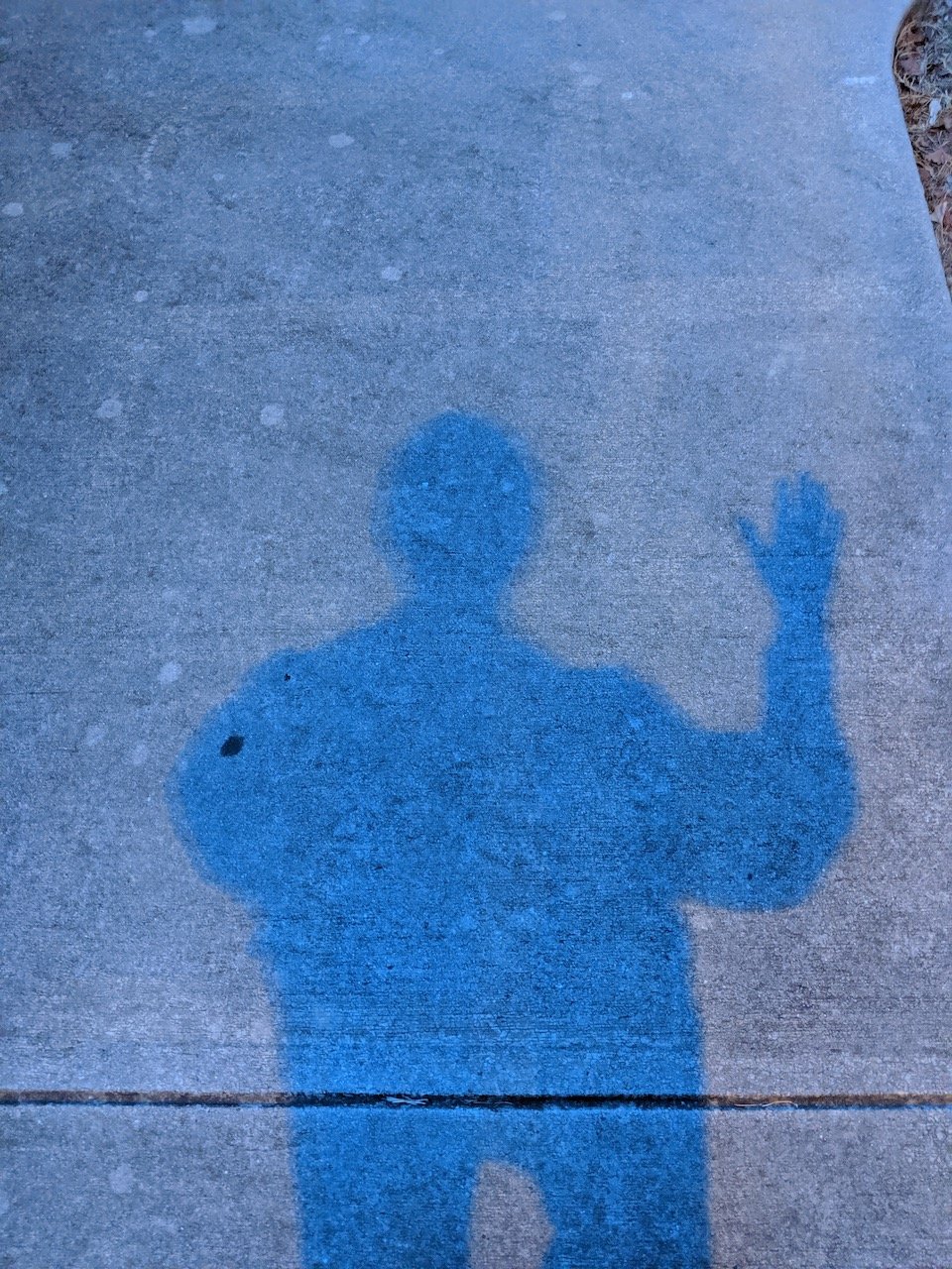 Shadow of standing figure with one arm raised as if waving hello